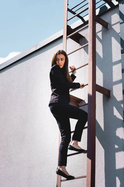 Scared businesswoman looking down while climbing stairs on rooftop — Stock Photo