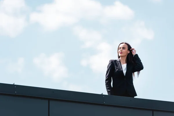 Attrayant femme d'affaires debout sur le toit, souriant et détournant les yeux — Photo de stock