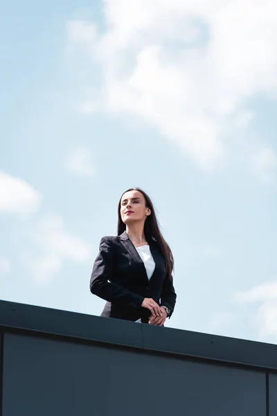 Attractive, confident businesswoman smiling and looking away while standing on rooftop — Stock Photo