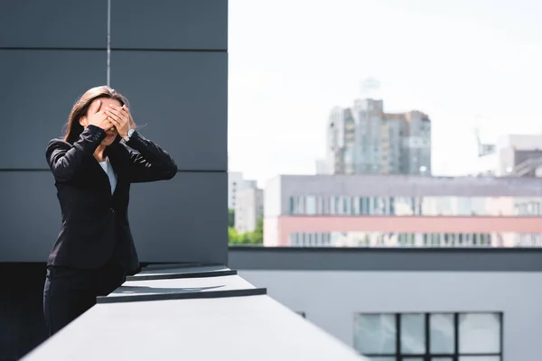 Young businesswoman, suffering from fear of heights, standing on rooftop and covering face with hands — Stock Photo