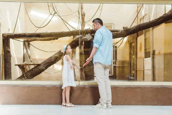 Cute daughter looking at father and showing shrug gesture in zoo — Stock Photo