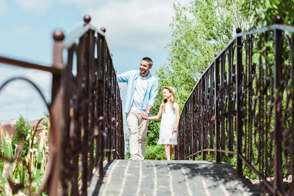 Messa a fuoco selettiva del padre che si tiene per mano con la figlia mentre cammina sul ponte — Foto stock