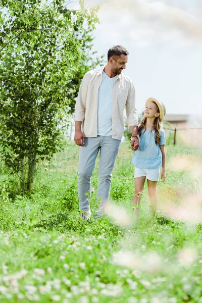 Selektiver Fokus von Vater und Tochter, die in der Nähe grüner Pflanzen gehen und sich an den Händen halten — Stockfoto