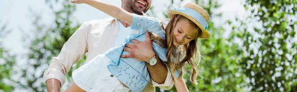 Panoramic shot of father holding in arms happy daughter in straw hat — Stock Photo