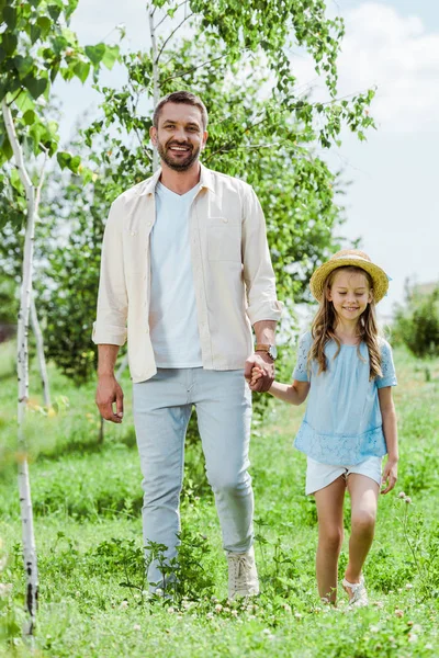 Feliz padre e hija de pie cerca de plantas verdes y tomados de la mano - foto de stock
