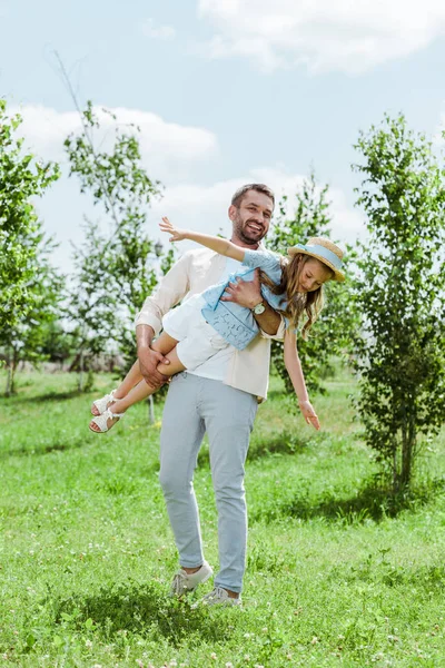 Feliz padre sosteniendo en brazos alegre hija en sombrero de paja - foto de stock