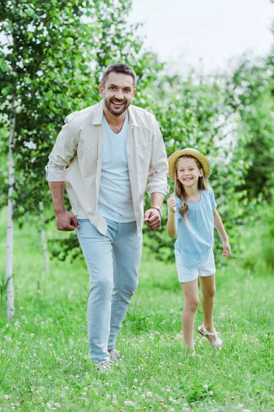 Nettes und glückliches Kind mit Strohhut gestikuliert neben fröhlichem Vater und schaut in die Kamera — Stockfoto