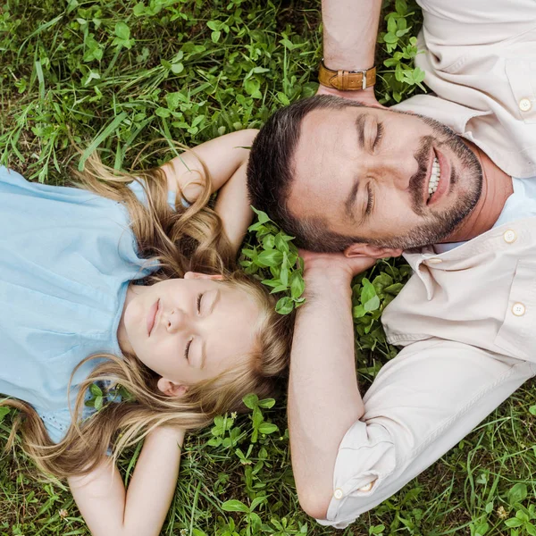 Draufsicht auf glücklichen Vater und niedliche Tochter, die auf grünem Gras liegen — Stockfoto