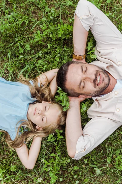 Vue de dessus du père joyeux et de la fille mignonne couchée sur l'herbe verte — Photo de stock
