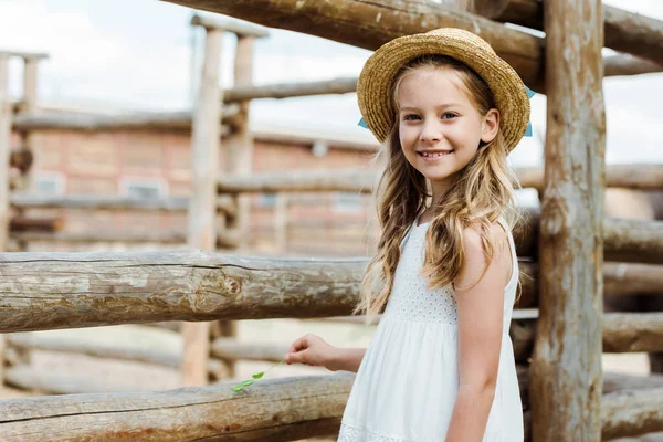 Happy kid in straw hat standing in white dress near fence in zoo — Stock Photo