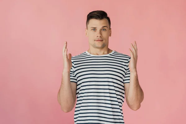 Front view of handsome young man with hands up in striped t-shirt looking at camera isolated on pink — Stock Photo