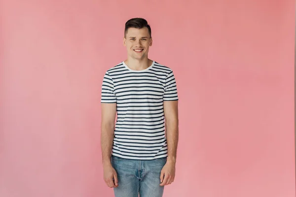 Vorderseite eines lächelnden, gut aussehenden jungen Mannes in gestreiftem T-Shirt, der isoliert auf rosa Kamera blickt — Stockfoto