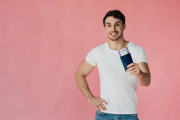 Vista frontale dell'uomo muscoloso sorridente in t-shirt bianca con passaporto e biglietto aereo isolato su rosa — Foto stock