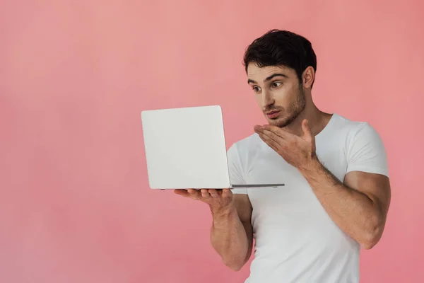 Homme musclé concentré en t-shirt blanc en utilisant un ordinateur portable isolé sur rose — Photo de stock