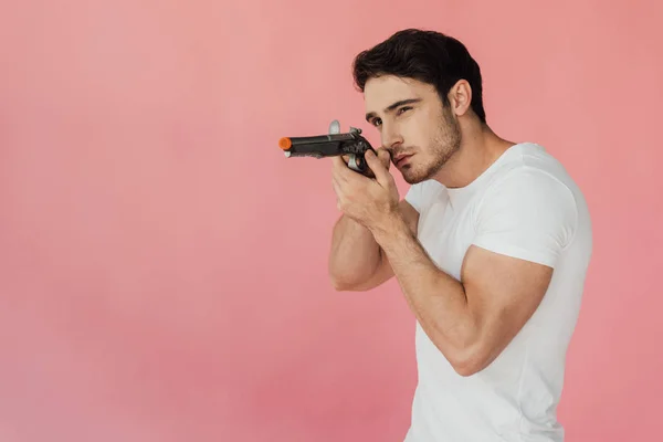 Muskulöser Mann im weißen T-Shirt zielte mit Pistole isoliert auf rosa — Stockfoto