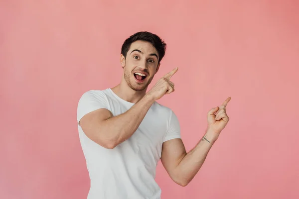 Excited muscular man in white t-shirt pointing with fingers isolated on pink — Stock Photo