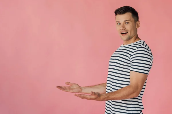 Smiling man in striped t-shirt pointing with hands isolated on pink — Stock Photo