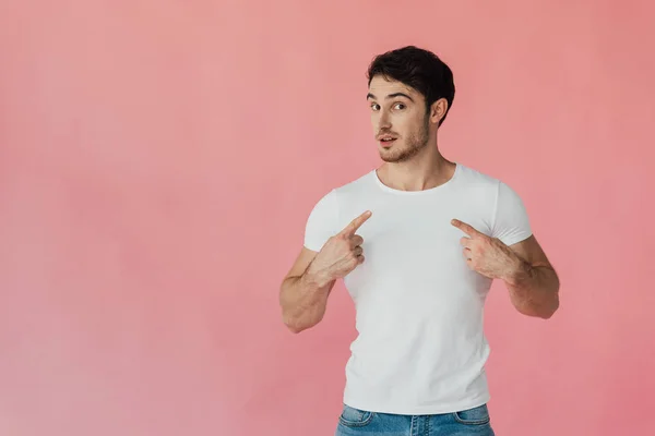 Hombre musculoso en camiseta blanca apuntando con los dedos a sí mismo aislado en rosa - foto de stock