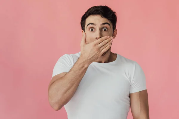 Vue de face de l'homme musclé choqué en t-shirt blanc couvrant la bouche avec la main isolée sur rose — Photo de stock