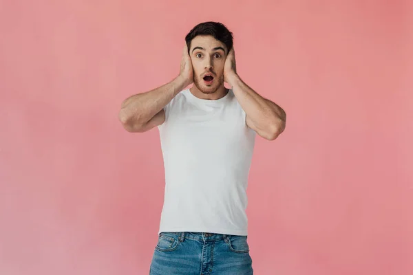 Front view of shocked muscular man in white t-shirt covering ears with hands isolated on pink — Stock Photo