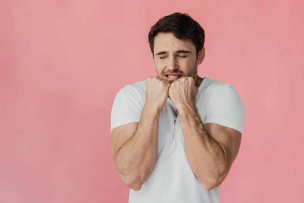 Hombre musculoso asustado en camiseta blanca sosteniendo puños cerca de la cara aislado en rosa - foto de stock