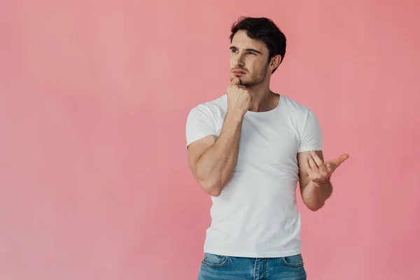 Uomo muscoloso pensoso in t-shirt bianca che appoggia il viso con pugno e conta sulle dita isolate su rosa — Foto stock