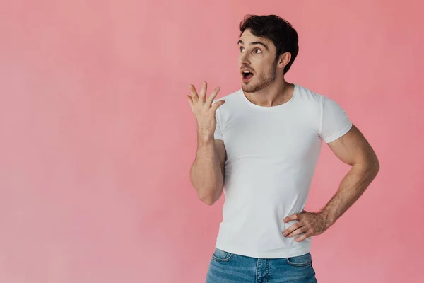 Amazed muscular man in white t-shirt standing with hand on hip and looking up isolated on pink — Stock Photo