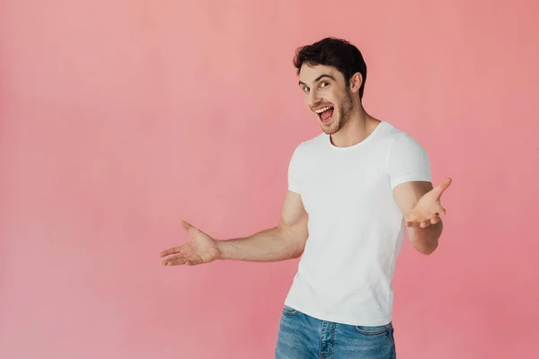 Aufgeregter muskulöser Mann in weißem T-Shirt winkt mit den Händen und blickt vereinzelt in die Kamera auf rosa — Stockfoto