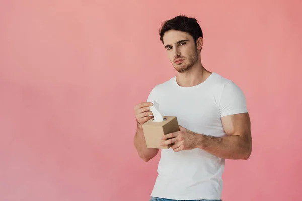 Hombre musculoso disgustado en camiseta blanca sosteniendo servilletas y mirando a la cámara aislada en rosa - foto de stock