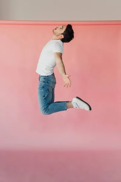 Muscular man in white t-shirt and jeans jumping on pink — Stock Photo