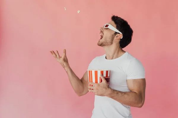 Muscular man in 3d glasses throwing up and eating popcorn isolated on pink — Stock Photo