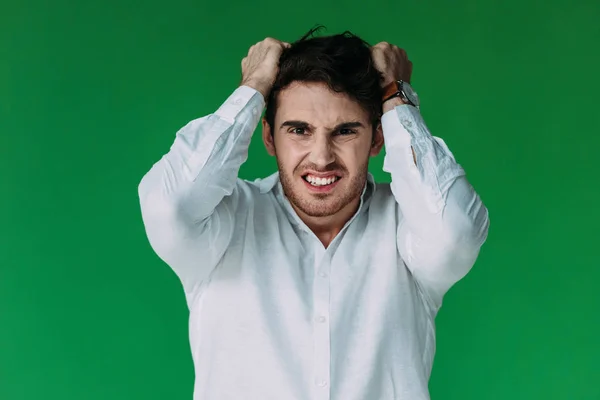 Vista frontal del hombre enojado en camisa blanca mirando a la cámara aislada en verde - foto de stock