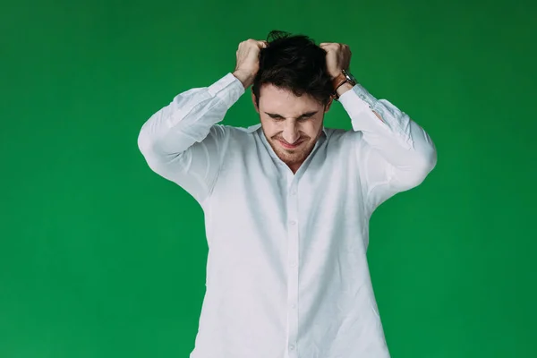 Vista frontal del hombre estresado en camisa blanca tocando el cabello aislado en verde - foto de stock