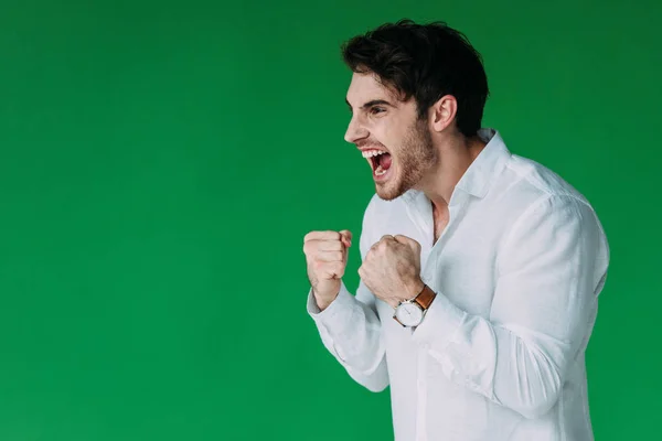 Uomo arrabbiato in camicia bianca tenendo i pugni e urlando isolato sul verde — Foto stock
