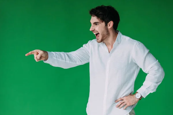 Hombre estresado en camisa blanca gritando y señalando con el dedo aislado en verde - foto de stock