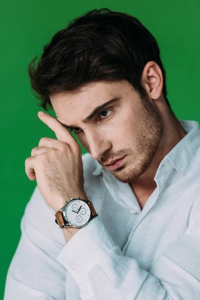 Серйозний чоловік у білій сорочці та наручний годинник, який торкається обличчя рукою ізольовано на зеленому — стокове фото