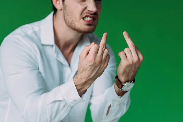 Vista recortada de hombre enojado en camisa blanca que muestra los dedos medios aislados en verde - foto de stock