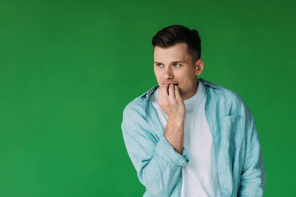 Беспокойный молодой человек в рубашке кусает пальцы и смотрит в сторону изолированы на зеленый — стоковое фото