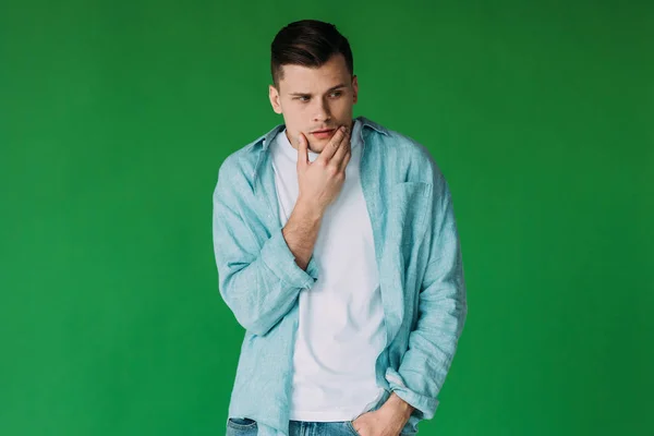 Pensive young man standing with hand in pocket and rubbing chin isolated on green — Stock Photo