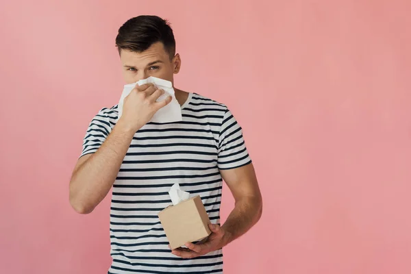 Young man in striped t-shirt wiping nose with napkin isolated on pink — Stock Photo