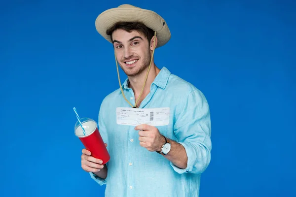 Smiling traveler in safari hat holding air ticket and beverage isolated on blue — Stock Photo