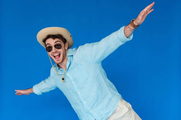 Turista excitado en sombrero de safari y gafas de sol riendo y agitando las manos aisladas en azul - foto de stock