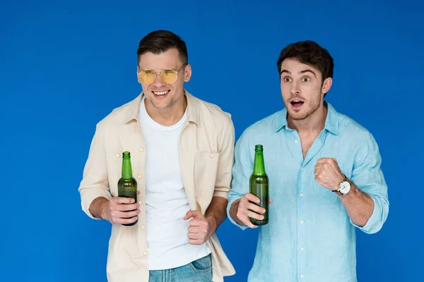 Два друга держат бутылки пива и смотрят в сторону изолированных на синий — стоковое фото