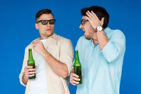 Deux amis inquiets dans des verres 3D tenant des bouteilles de bière et se regardant isolés sur bleu — Photo de stock