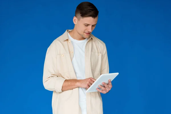 Молодий чоловік у сорочці за допомогою цифрового планшета ізольований на синьому — стокове фото
