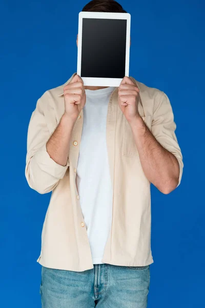 Vista frontal del joven en camisa sosteniendo tableta digital con pantalla en blanco aislado en azul - foto de stock