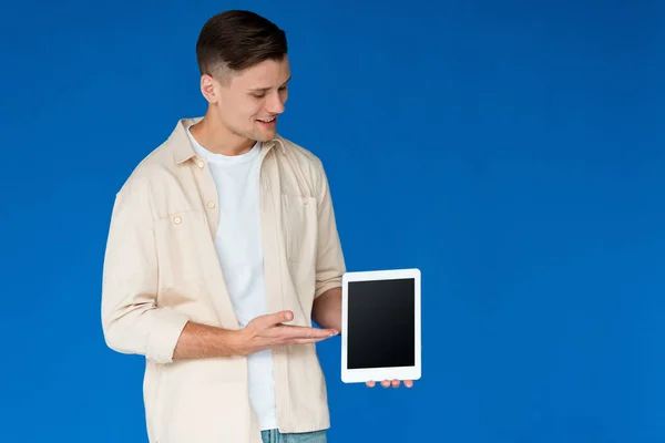 Lächelnder junger Mann im Hemd mit digitalem Tablet und leerem Bildschirm, isoliert auf blau — Stockfoto