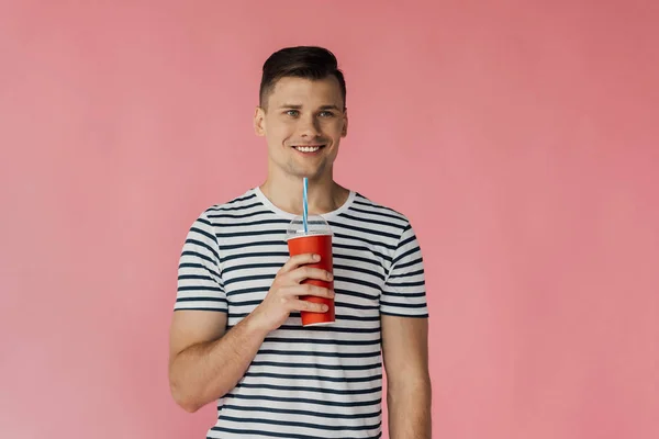 Front view of smiling young man in striped t-shirt holding beverage isolated on pink — Stock Photo