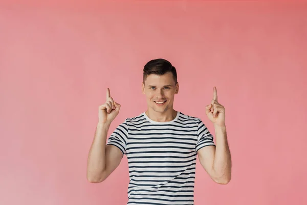 Front view of smiling young man in striped t-shirt showing idea signs isolated on pink — Stock Photo