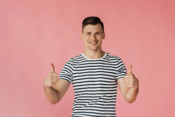 Front view of smiling young man in striped t-shirt showing thumbs up isolated on pink — Stock Photo